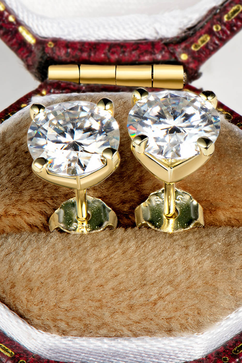 Gold moissanite solitaire stud earrings with sculpted settings in a jewelry box.