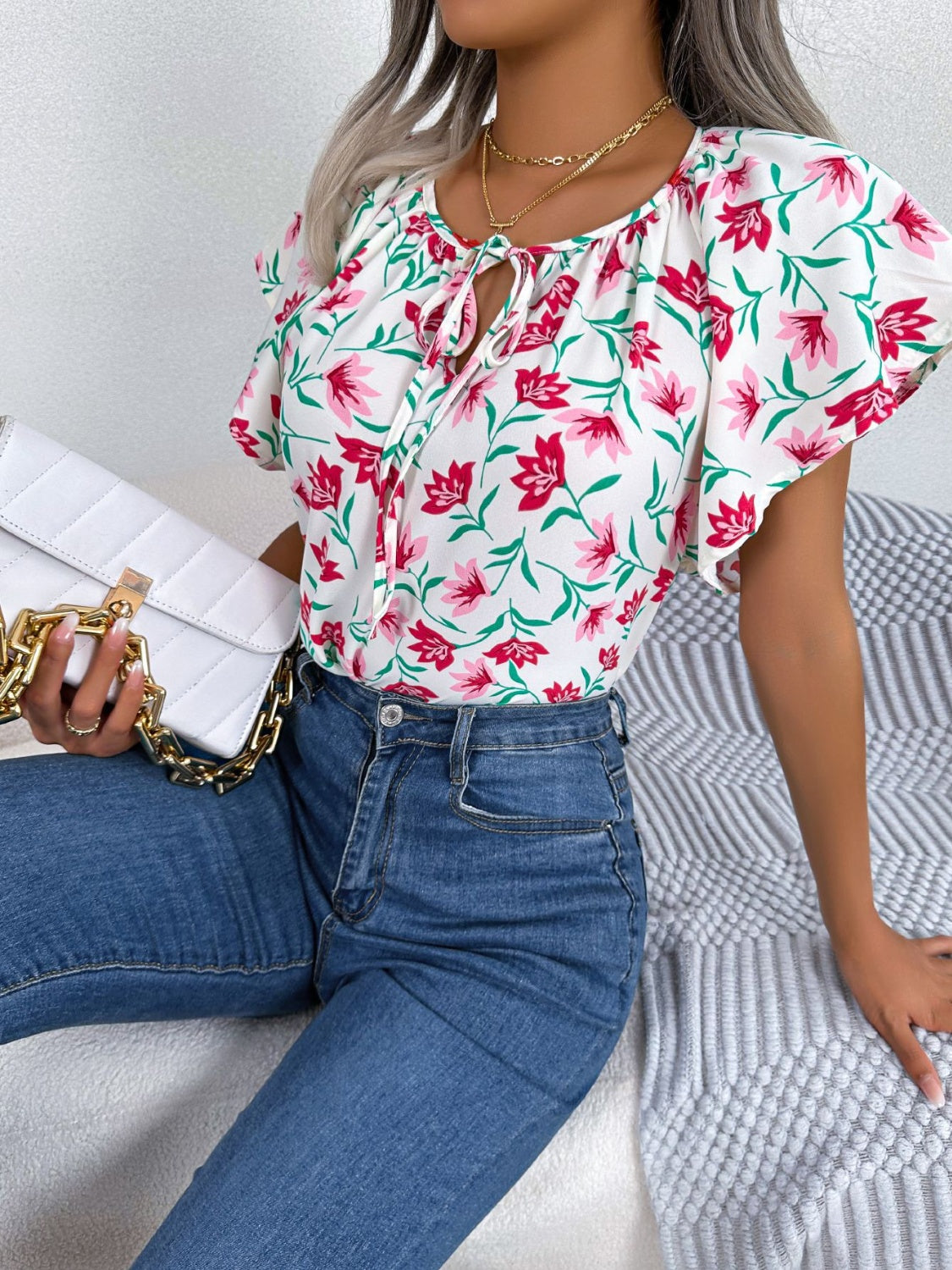 White floral ruffle sleeve tie-neck blouse with pink flowers and green leaves.