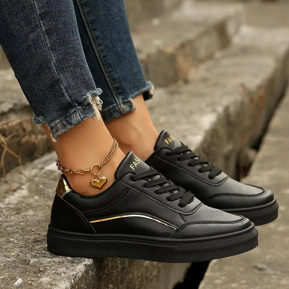 Black sneakers with gold metallic trim and heel accent, featuring a heart charm anklet.