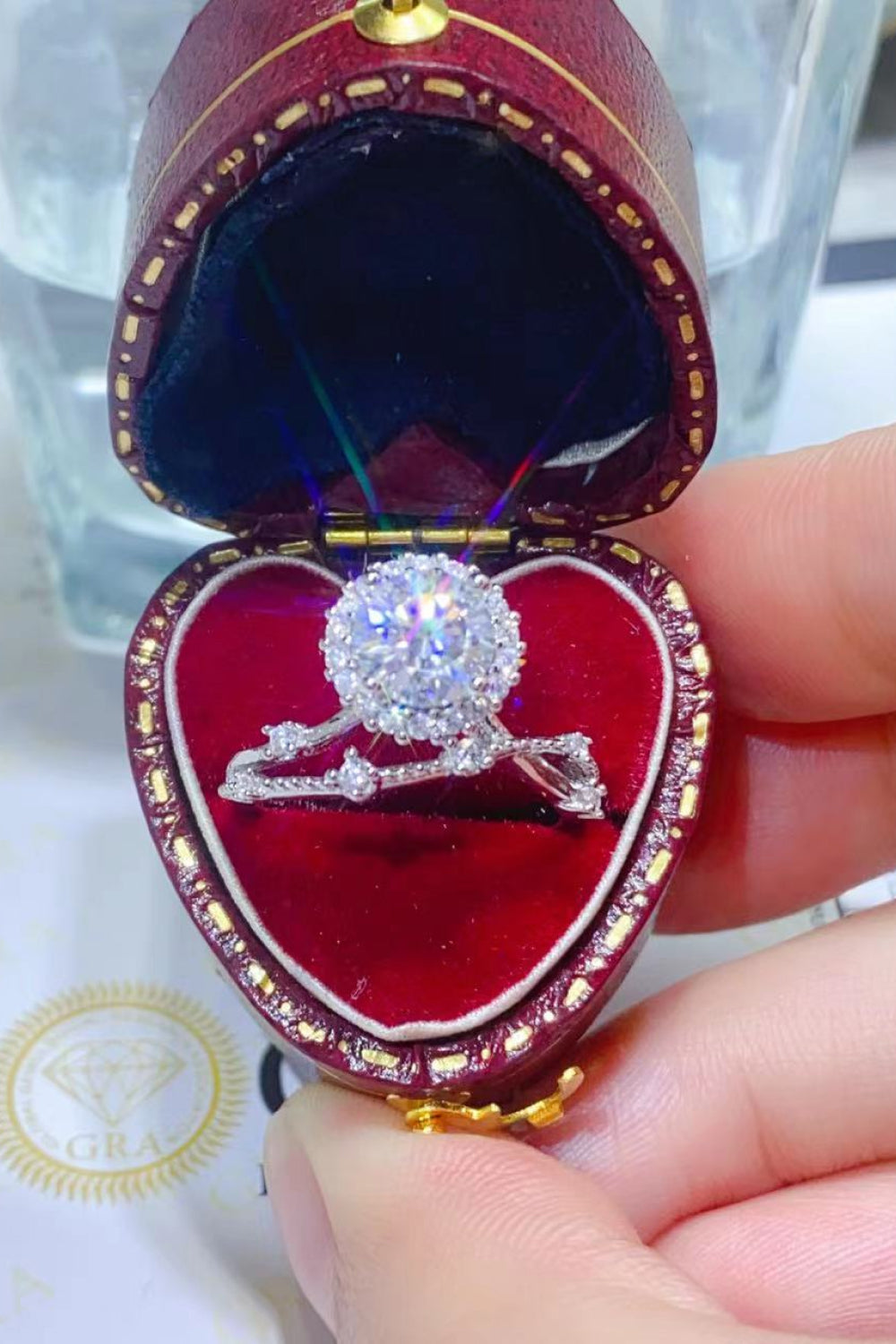 Diamond halo ring with a split band in a red heart-shaped jewelry box