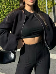 Black cropped bomber jacket with zip closure and voluminous sleeves, worn over a black crop top.