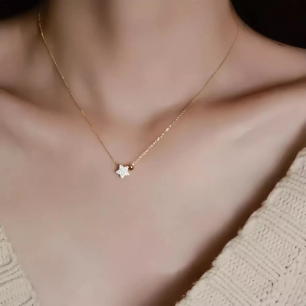 Gold necklace with a sparkling star pendant and a small bead detail.