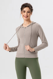 Tan zip-up hoodie with drawstrings and front pocket, styled with green leggings.