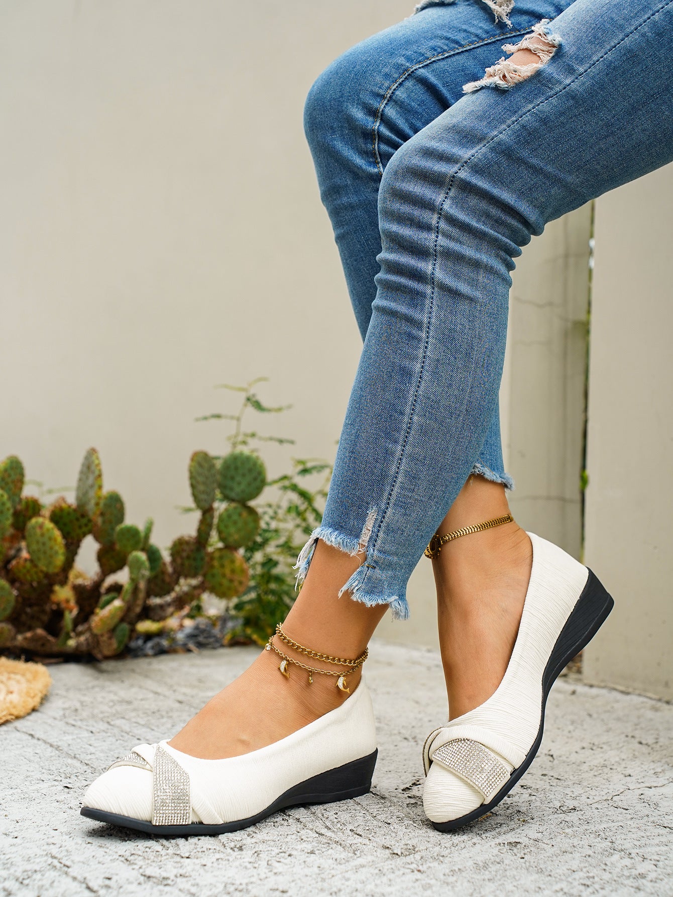 Beige slip-on wedge flats with rhinestone bow detail and textured upper.