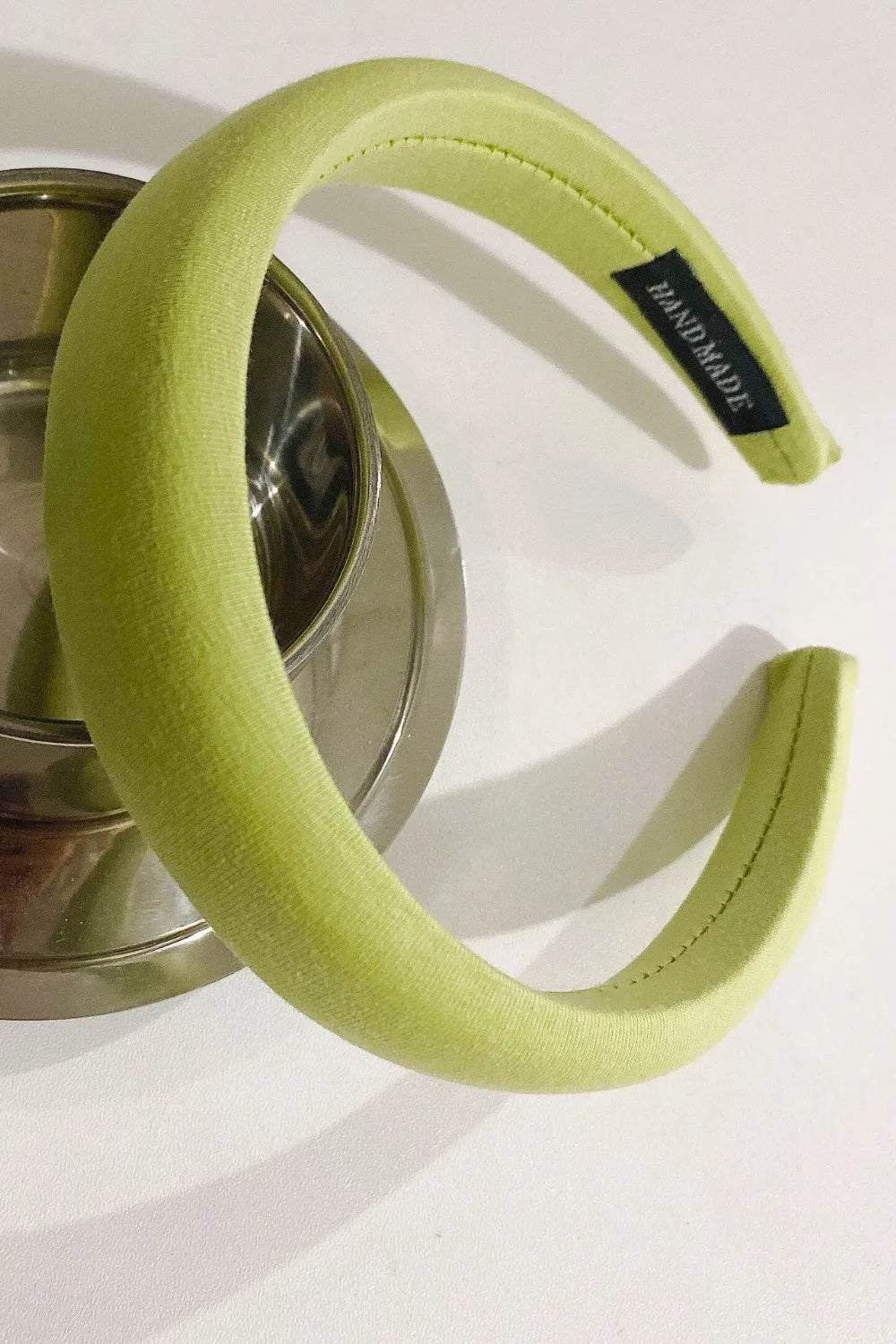 Padded headband in Matcha Green textured fabric with a black "HANDMADE" tag.