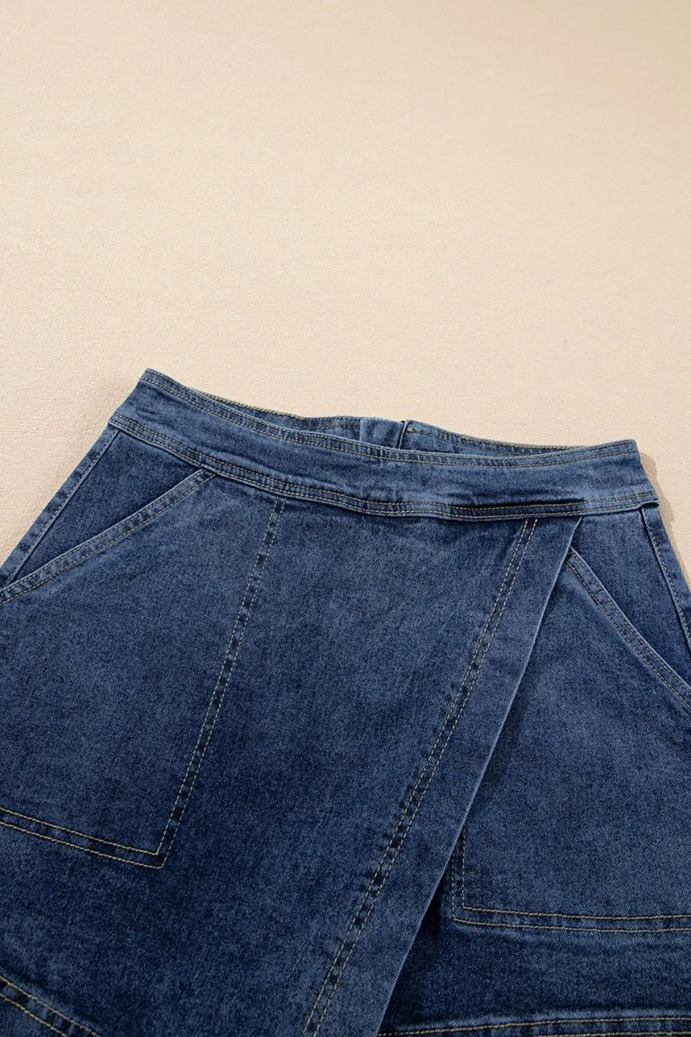 Denim wrap skort in medium wash with asymmetrical hem and patch pockets.