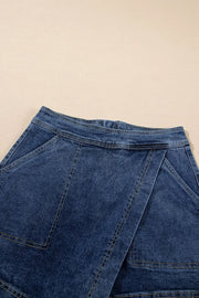 Denim wrap skort in medium wash with asymmetrical hem and patch pockets.