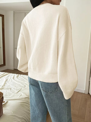 White V-neck knit sweater with balloon sleeves and ribbed hem, styled with jeans.