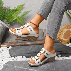 Chic white open-toe wedge sandals with gold buckle details and a textured sole.