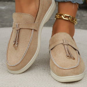 Khaki flat slip-ons with decorative strap and white piping detail.