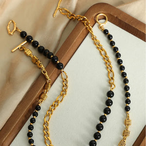 Gold asymmetrical beaded chain necklace with black beads and toggle clasp.