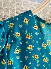 Teal floral midi dress with V-neck and short sleeves, featuring a yellow and purple floral print.
