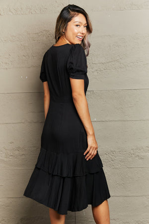 Black viscose wrap dress with button detail, puff sleeves, and tiered ruffled hem.