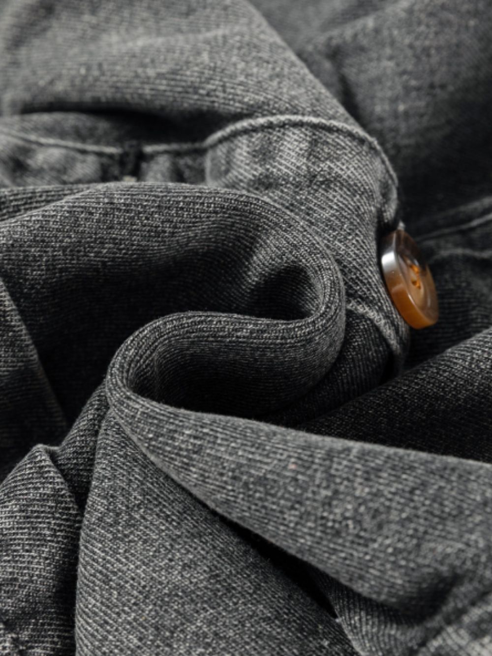 Faded gray denim pinafore dress detail showing button closure and textured fabric.