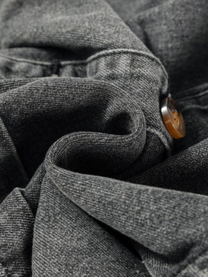 Faded gray denim pinafore dress detail showing button closure and textured fabric.
