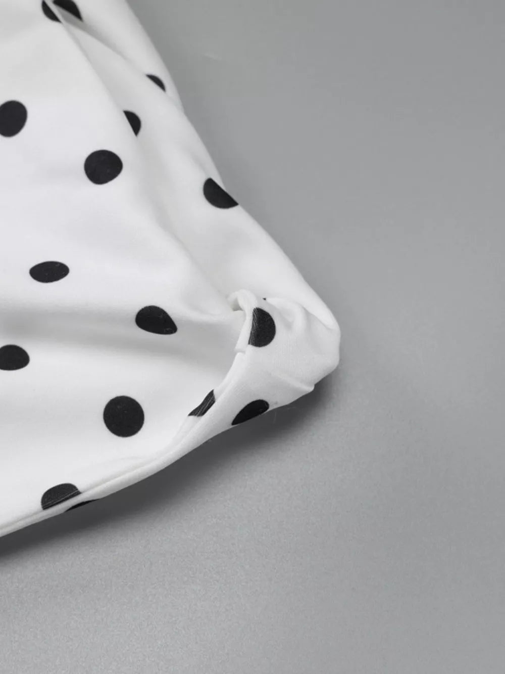 White polka dot mini dress with asymmetrical hem and bow detail.