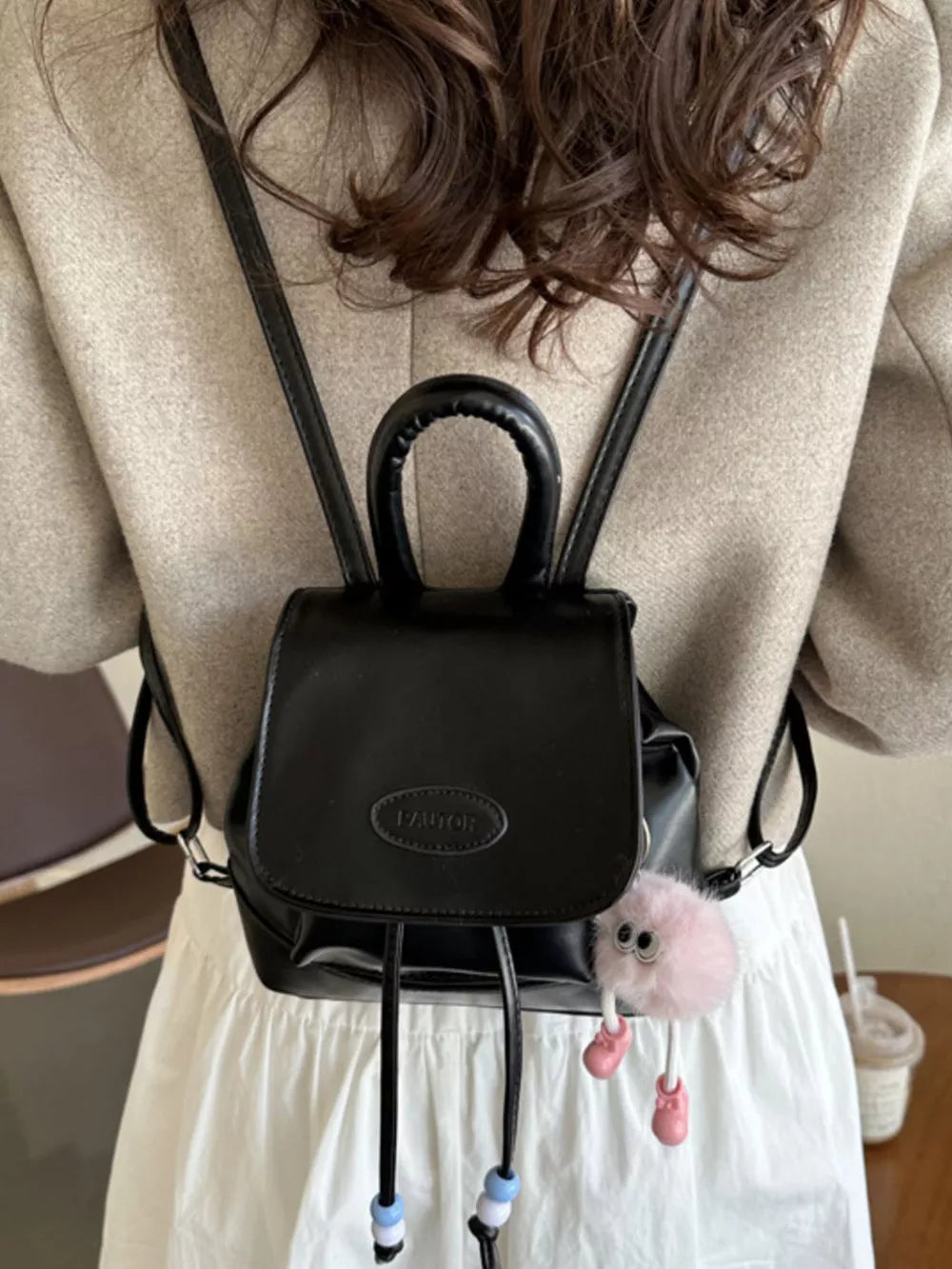 Black mini leather drawstring backpack with beaded details and a fluffy charm