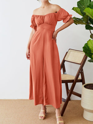 Off-the-shoulder ruched coral jumpsuit with a cinched waist and wide legs.