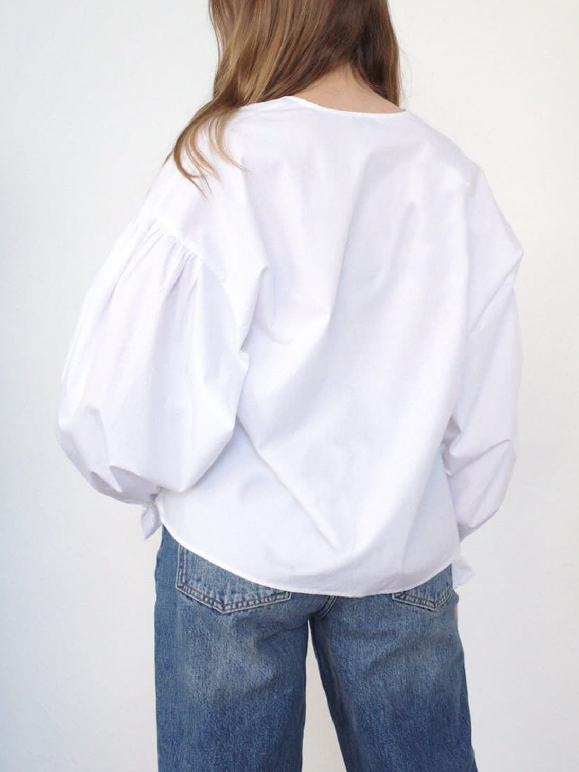 White long sleeve blouse with voluminous puff sleeves and a tie detail at the hem.