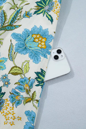 Floral cotton mini dress with a white background, blue and yellow flowers, and a pocket holding a smartphone.