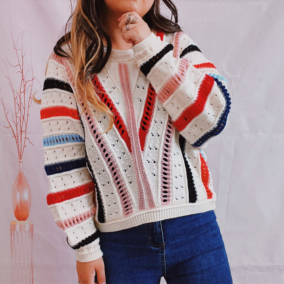 Colorblock openwork knit sweater with V-shaped stripes in red, pink, and black on a white base.