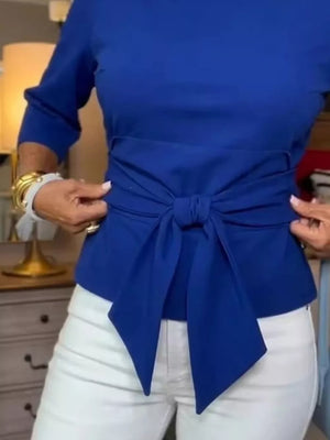 Blue 3/4 sleeve t-shirt with a chic tied waist detail, worn with white pants.