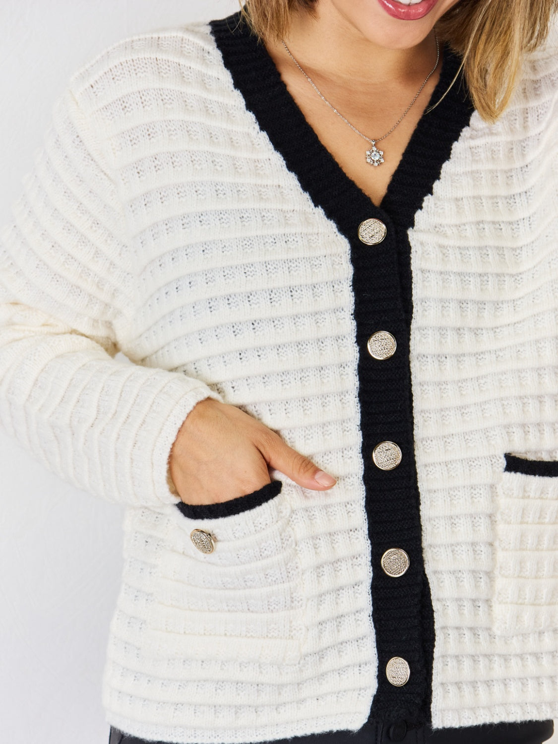 White textured knit cardigan with black contrast trim and buttons, featuring patch pockets.