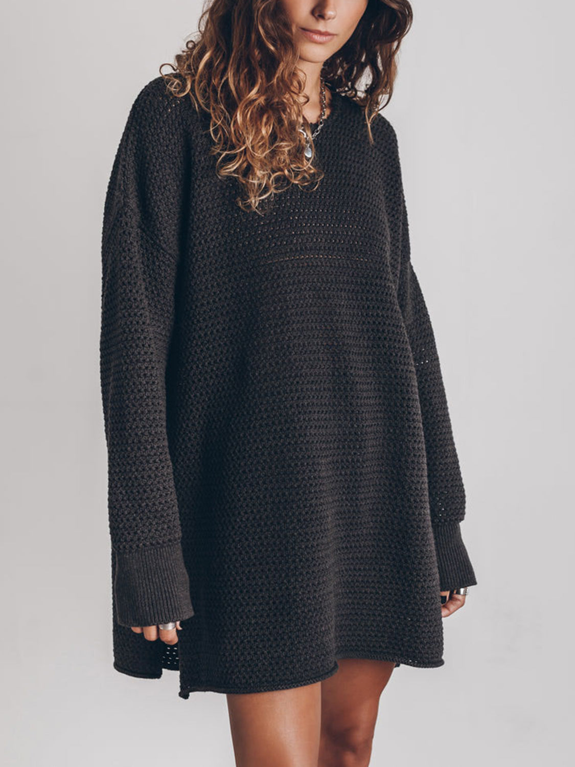 Oversized black open-knit sweater dress with crew neck and long sleeves.
