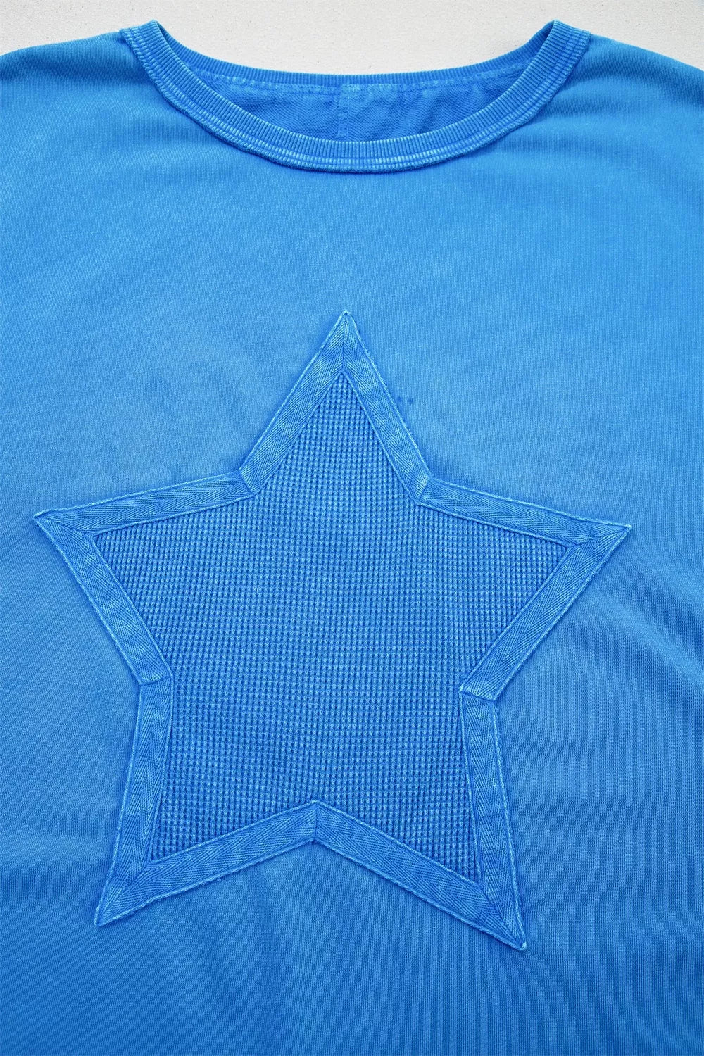 Blue mineral wash cotton tee with a textured star patch and raw edge neckline.