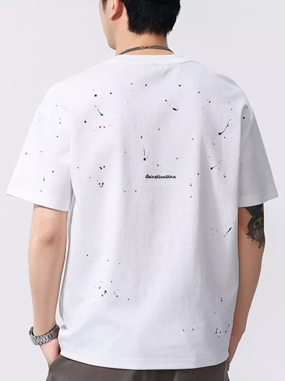 White cotton t-shirt with black and red paint splatter detail and subtle text graphic.