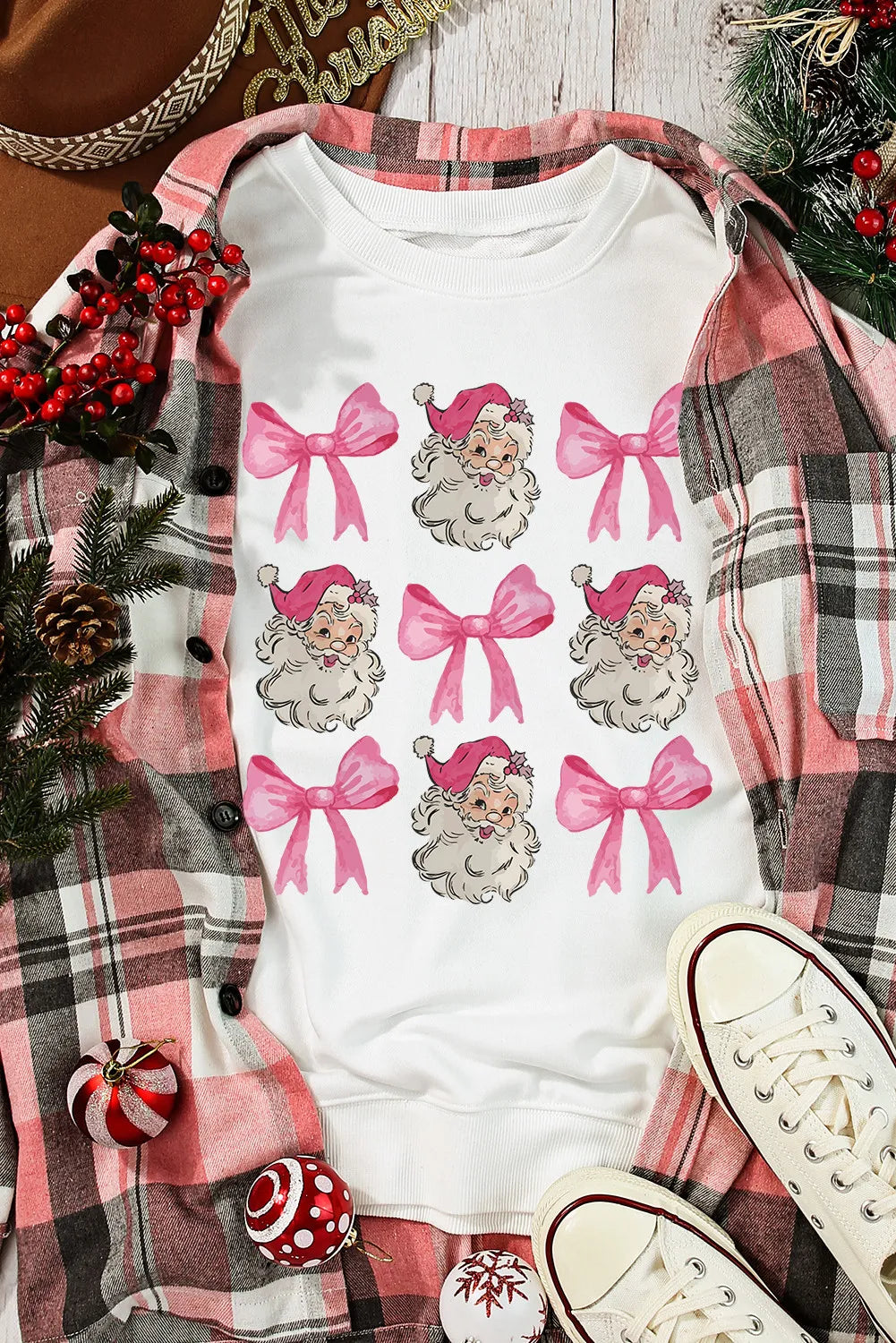 White crewneck sweatshirt with a repeating pattern of Santa faces and pink bows.