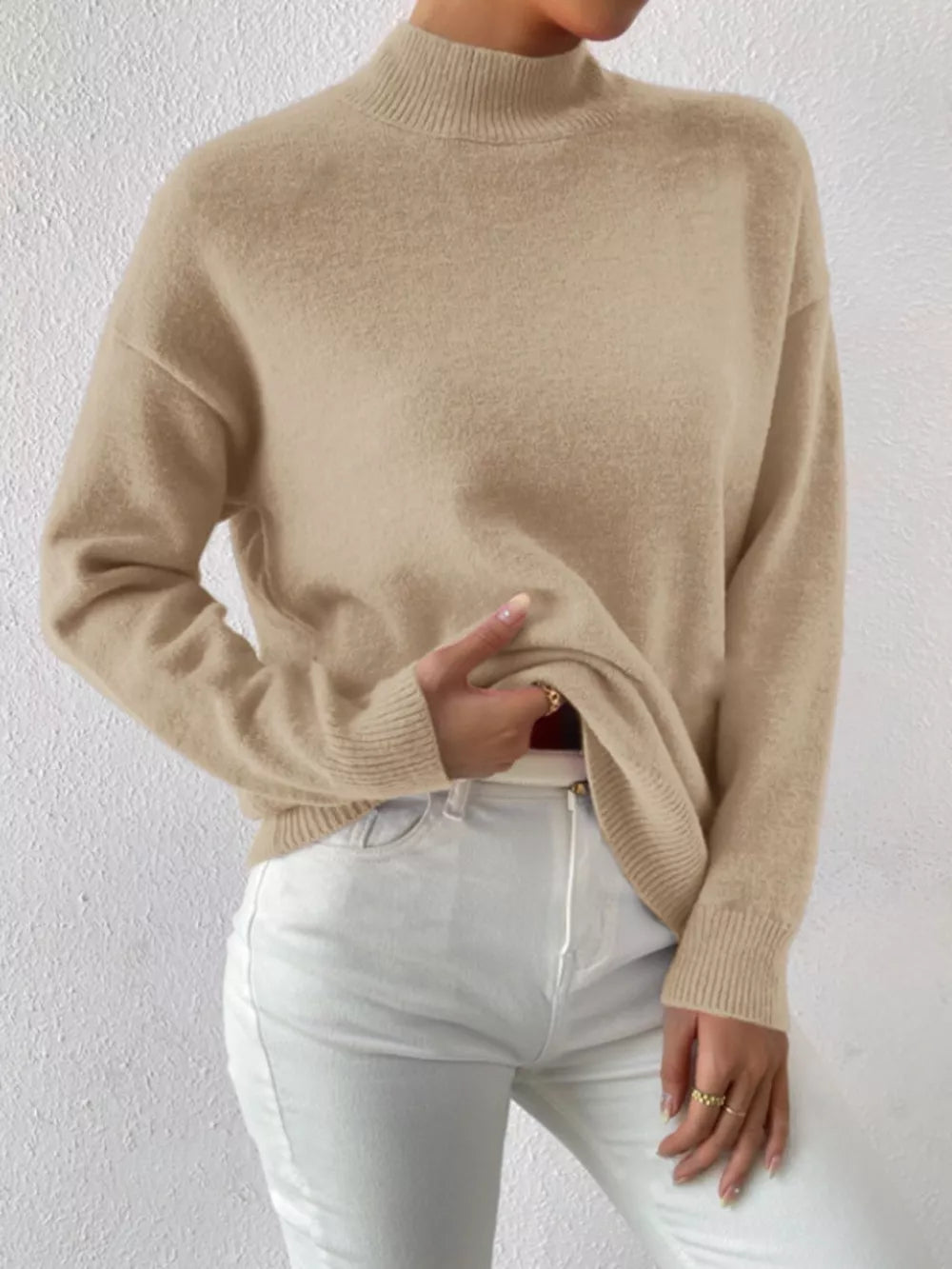 Khaki mock neck knit sweater with dropped shoulders, styled with white jeans.