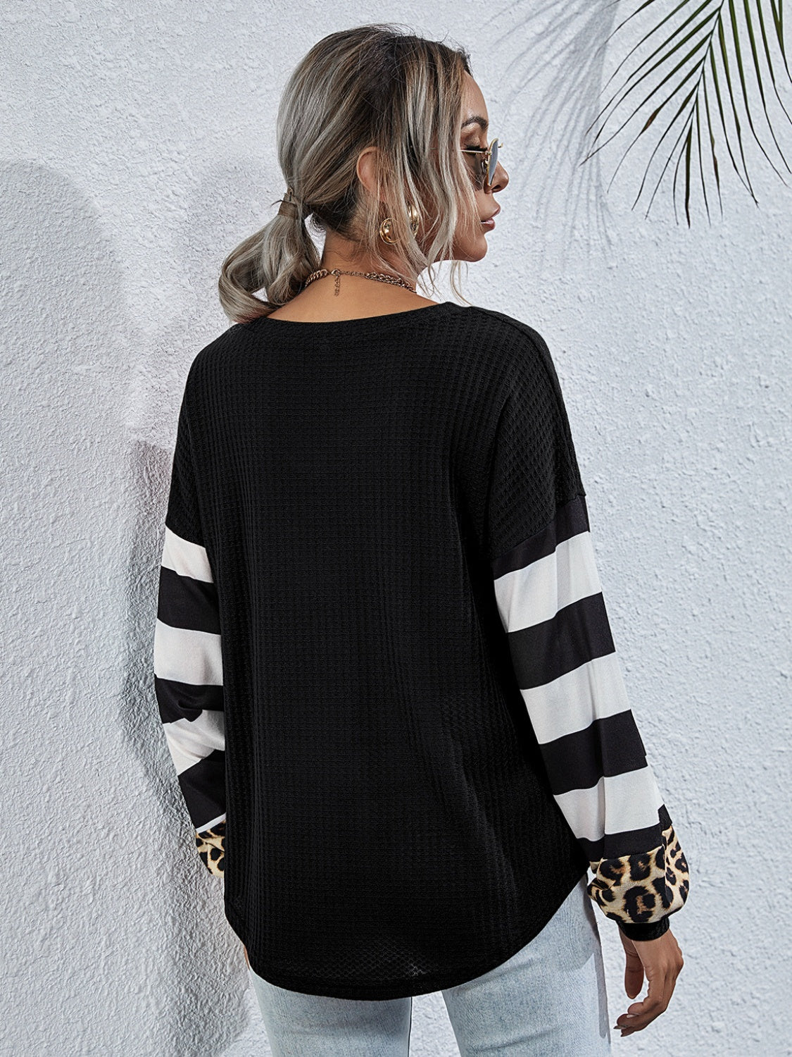 Black waffle knit top with striped and leopard print sleeves.