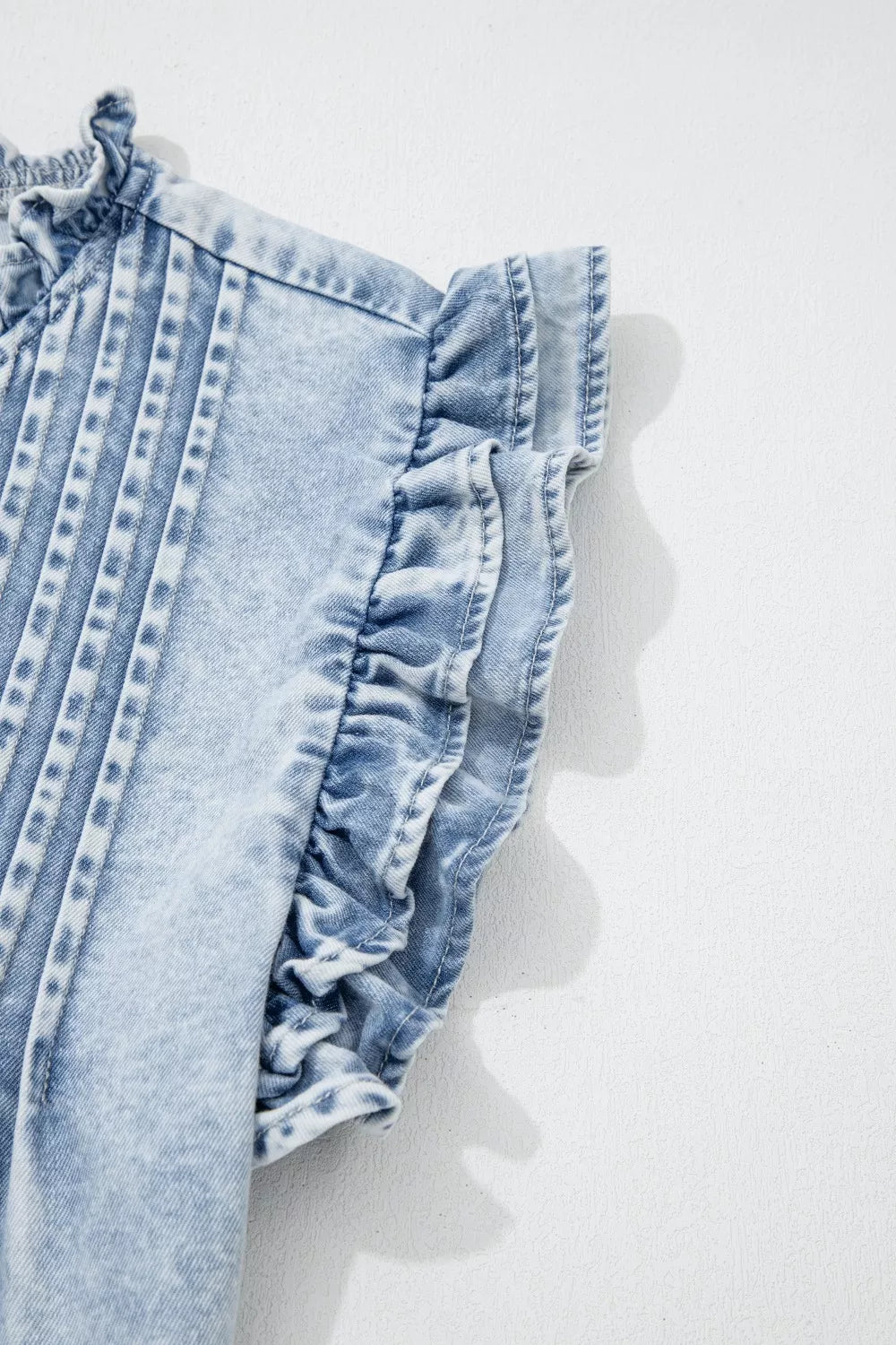 Light wash denim top with ruffled cap sleeves and pintuck details.