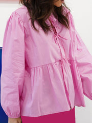 Pink tie-front peplum blouse with voluminous sleeves and a ruffled hem.