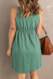 Green button-down mini dress with gathered waistline and sleeveless design.