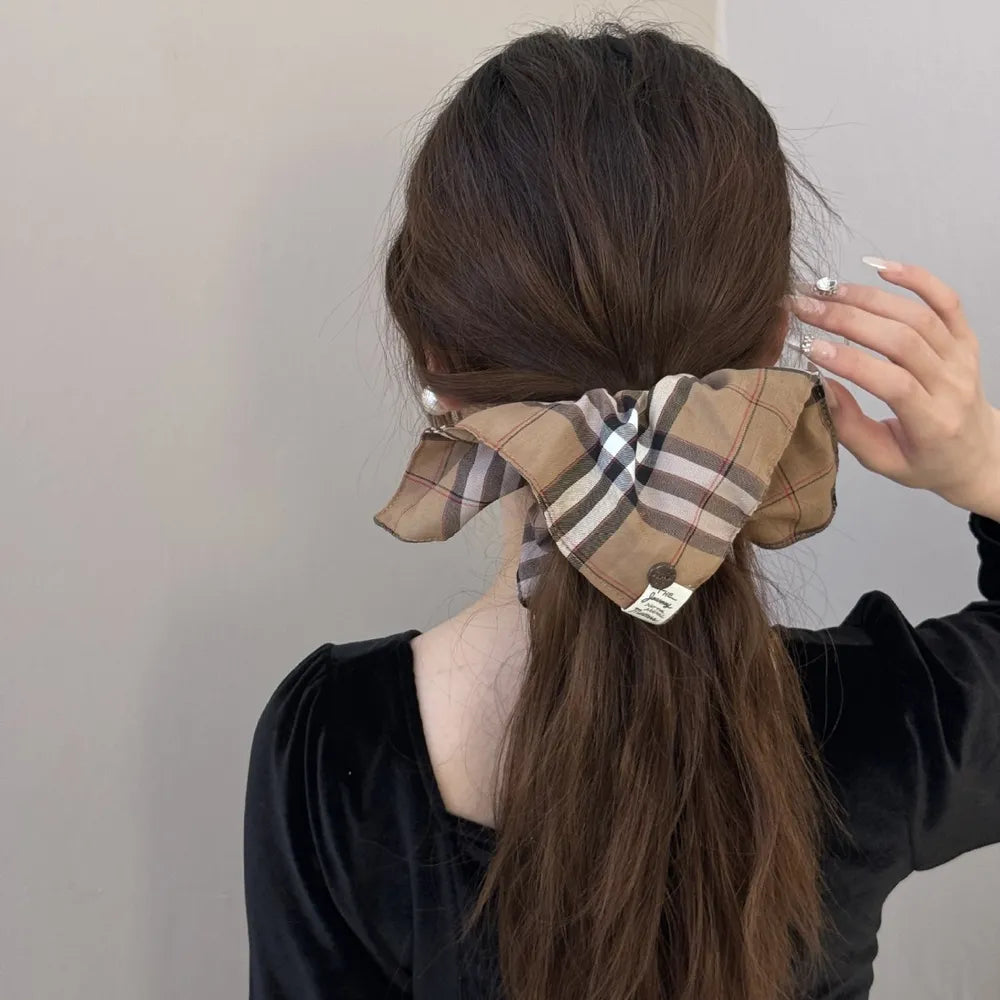 Plaid bow-tie scrunchie in camel with button detail on a ponytail.