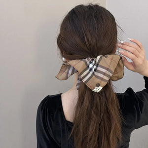 Plaid bow-tie scrunchie in camel with button detail on a ponytail.