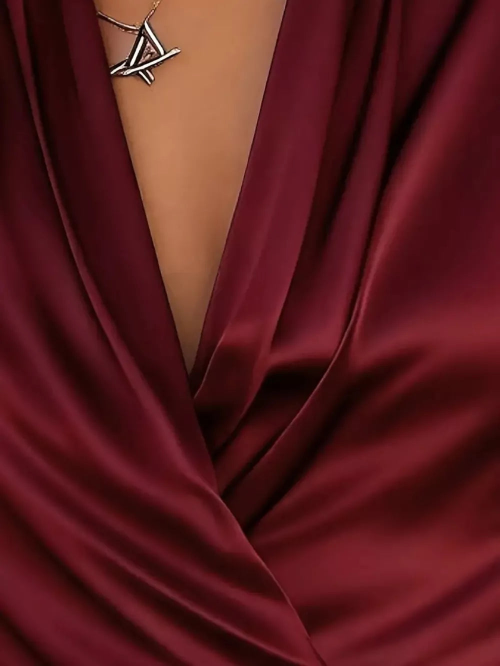 Wine red satin surplice blouse with draped neckline and geometric pendant necklace.