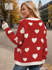 Red acrylic knit cardigan with white intarsia hearts and cream trim.
