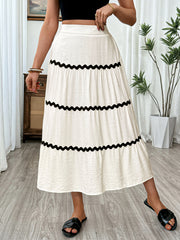 White tiered midi skirt with black wavy trim and textured fabric.