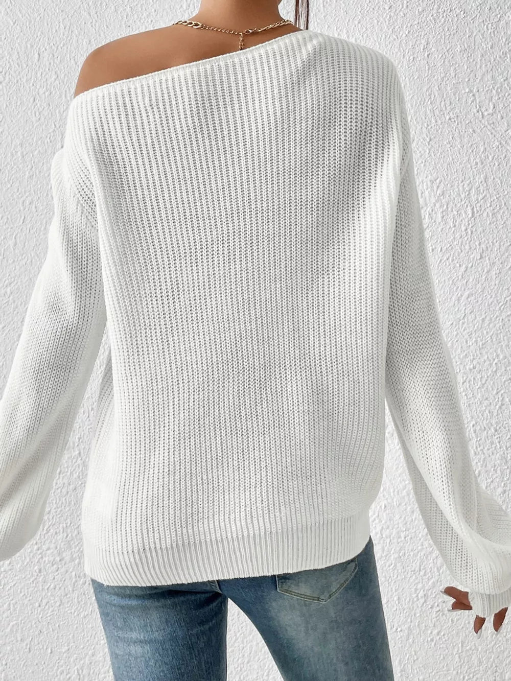 White asymmetrical knit sweater with off-shoulder neckline and long sleeves.