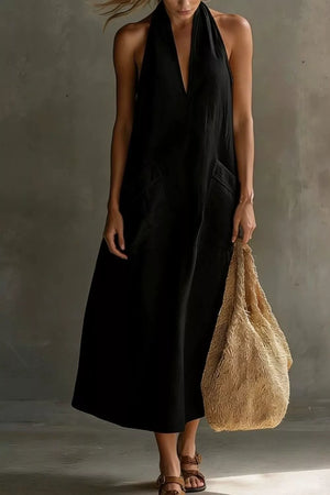 Black halter midi dress with pockets and deep V-neck, styled with sandals and a straw bag.