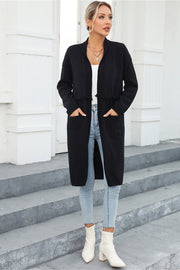 Black longline knit cardigan with fringe trim and pockets, worn open over a white top.