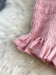 Pink eyelet crop top with ruffled hem and smocked detail.