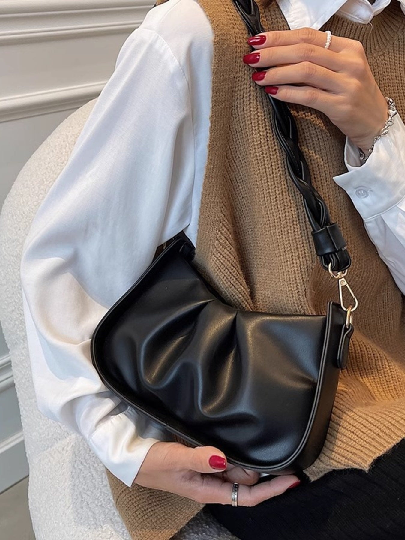 Black ruched crossbody bag with braided strap and gold hardware.