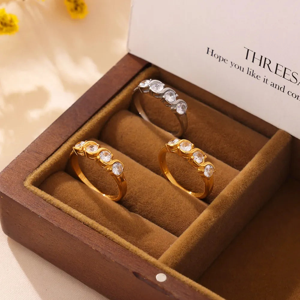 Gold and silver band rings with wave-set cubic zirconia stones in a jewelry box.