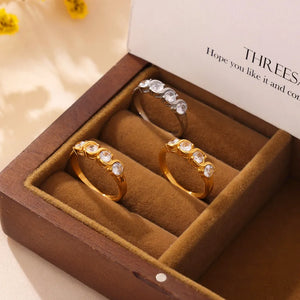 Gold and silver band rings with wave-set cubic zirconia stones in a jewelry box.