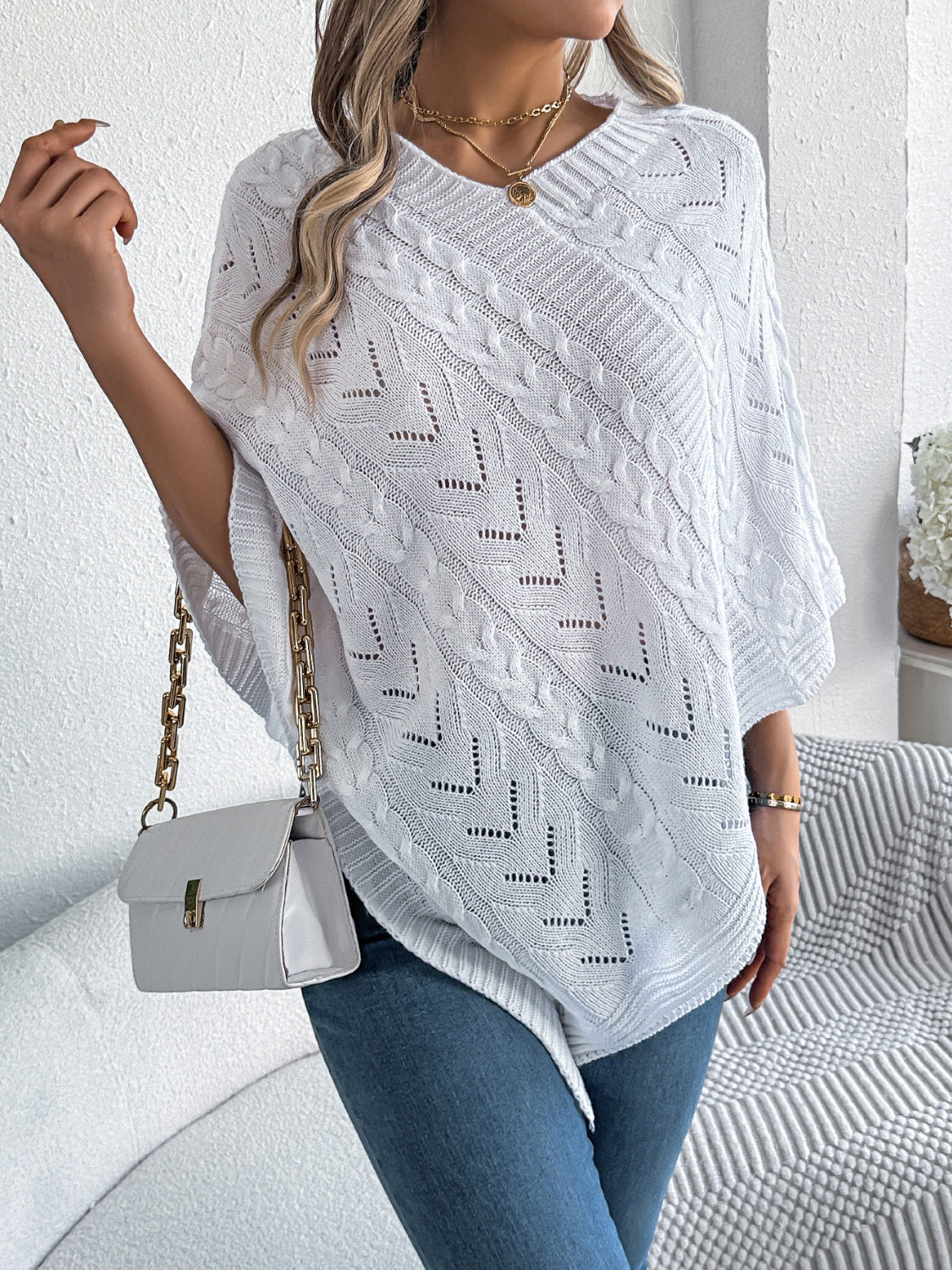 White cable knit poncho with chevron detail and V-neck, styled with a white crossbody bag.