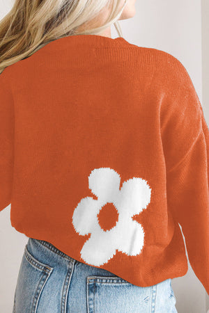 Orange acrylic crewneck sweater with white floral intarsia pattern detail.